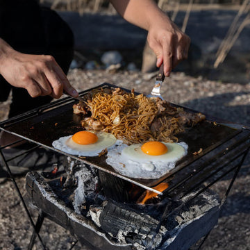 MAAGZ 料理鐵板搭配營火使用，露營早餐煎鐵板麵、蛋與肉片的戶外料理畫面